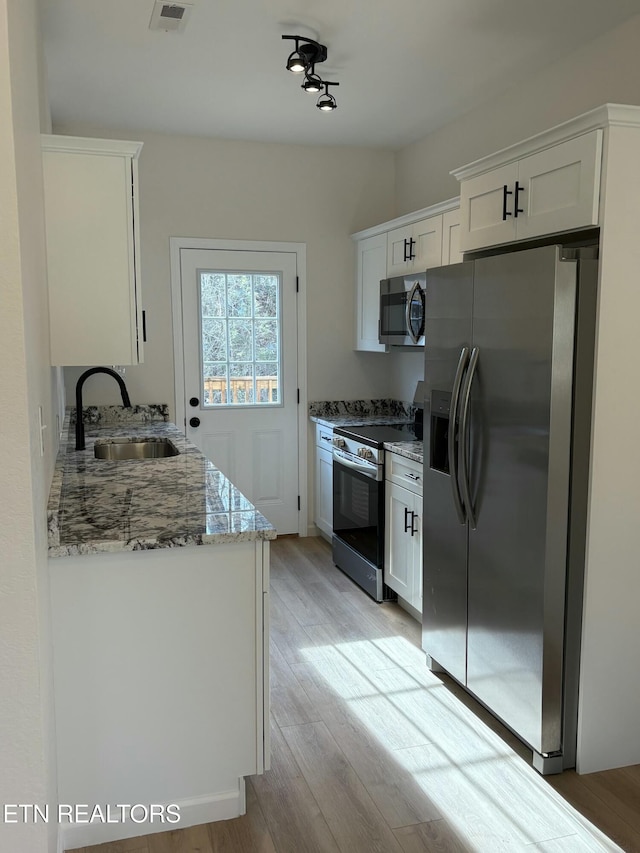 kitchen with a sink, light wood-type flooring, appliances with stainless steel finishes, and white cabinetry