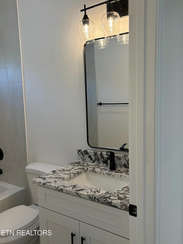 full bathroom with toilet, tub / shower combination, vanity, and a textured wall