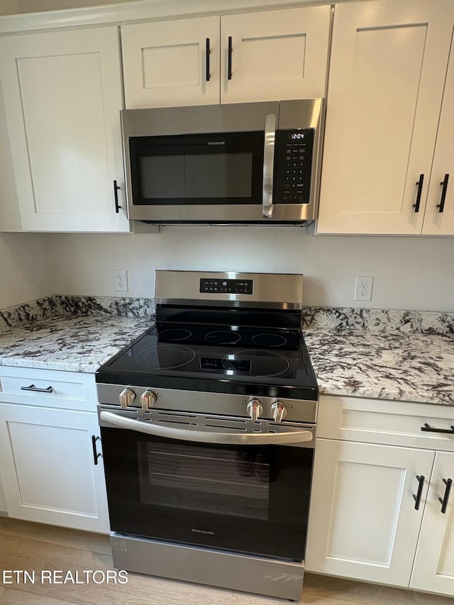 kitchen featuring stainless steel appliances, light stone countertops, and white cabinetry