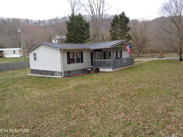 view of front of house with a porch, a wooded view, a front yard, and metal roof