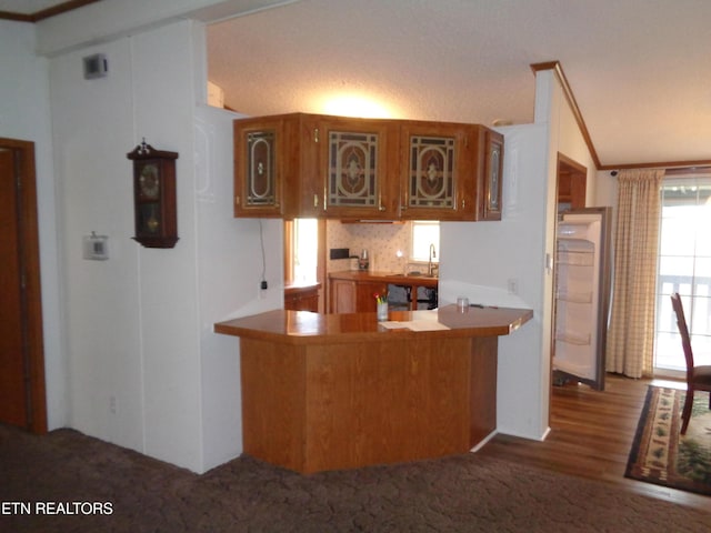 kitchen featuring glass insert cabinets, ornamental molding, brown cabinets, a peninsula, and a sink