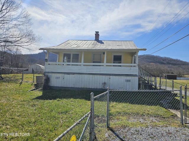 rear view of house featuring a standing seam roof, fence, a yard, metal roof, and a chimney