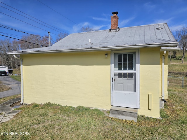 back of house featuring fence, stucco siding, a chimney, metal roof, and a yard