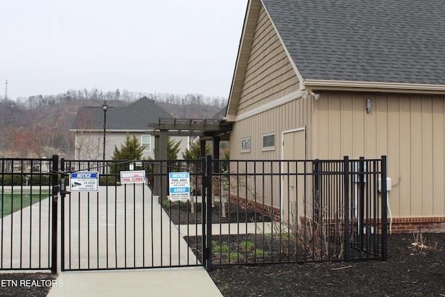 view of side of home featuring fence, roof with shingles, and a gate