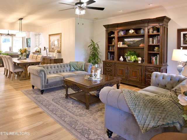 living room with light wood finished floors, crown molding, and a ceiling fan