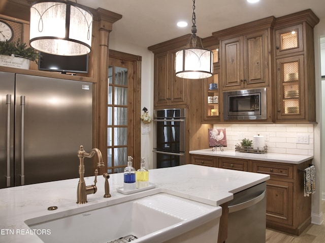 kitchen featuring brown cabinetry, a sink, built in appliances, pendant lighting, and tasteful backsplash