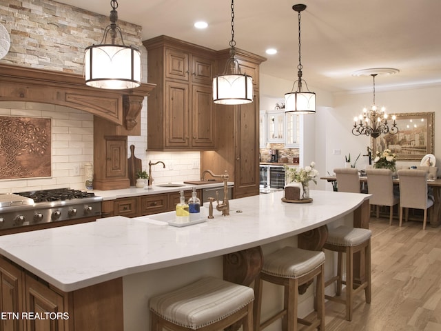 kitchen with backsplash, light stone countertops, stainless steel gas cooktop, light wood-type flooring, and a kitchen island with sink