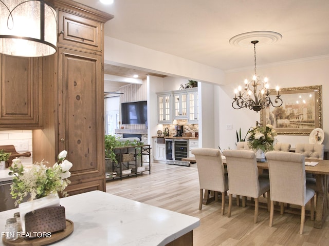 dining room featuring an inviting chandelier, wine cooler, light wood-style flooring, and crown molding