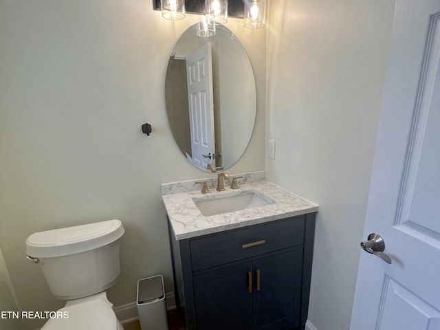 half bath featuring toilet, vanity, and baseboards