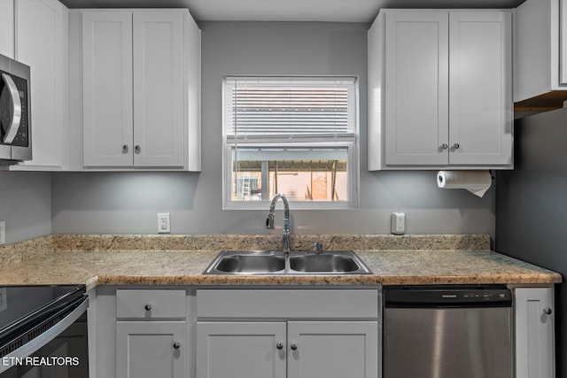 kitchen featuring appliances with stainless steel finishes, white cabinetry, light countertops, and a sink