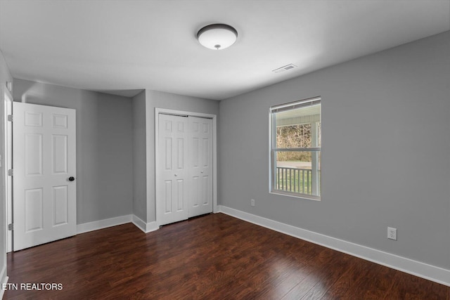 unfurnished bedroom with a closet, baseboards, visible vents, and dark wood-style floors