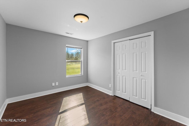 unfurnished bedroom featuring a closet, baseboards, visible vents, and wood finished floors