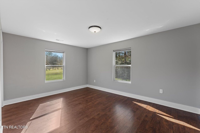 unfurnished room with visible vents, dark wood-style floors, and baseboards