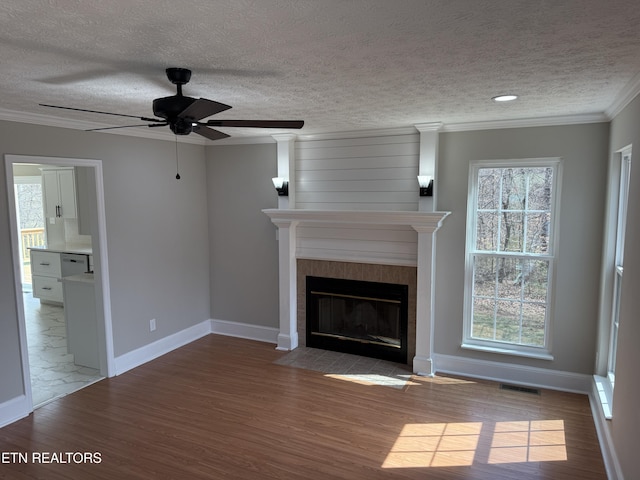 unfurnished living room with wood finished floors, a ceiling fan, visible vents, plenty of natural light, and a fireplace