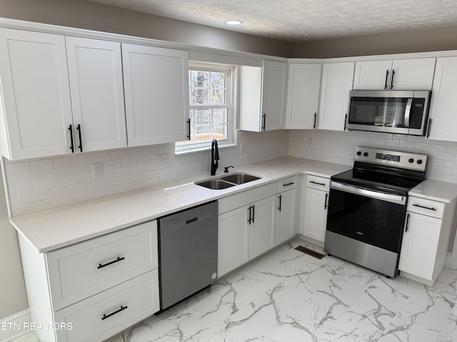 kitchen featuring a sink, stainless steel appliances, white cabinets, marble finish floor, and tasteful backsplash