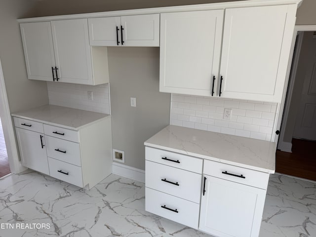 kitchen with light stone counters, marble finish floor, white cabinets, and baseboards