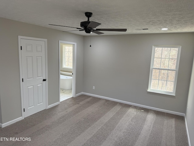 carpeted spare room featuring baseboards, a textured ceiling, a healthy amount of sunlight, and a ceiling fan