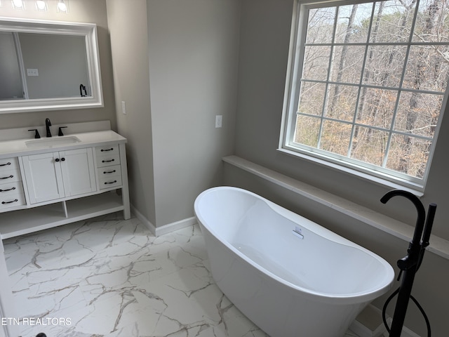 bathroom with marble finish floor, vanity, baseboards, and a freestanding tub