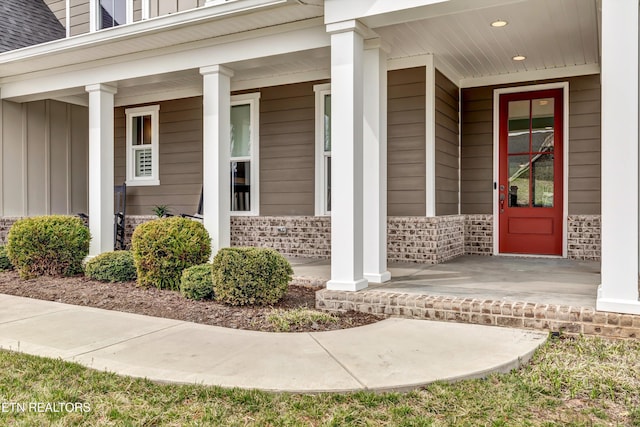 doorway to property featuring brick siding, a porch, and board and batten siding