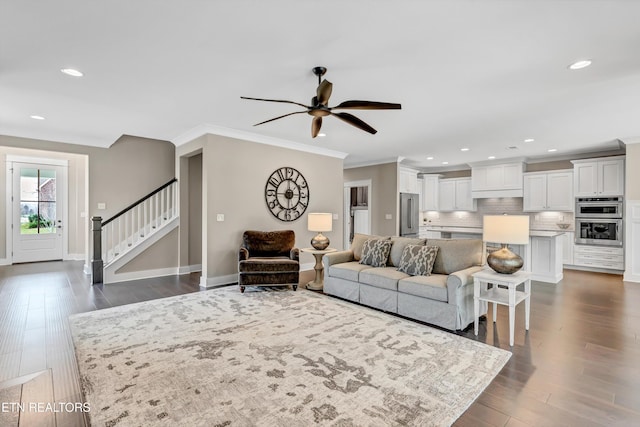 living area with ornamental molding, a ceiling fan, dark wood finished floors, baseboards, and stairs