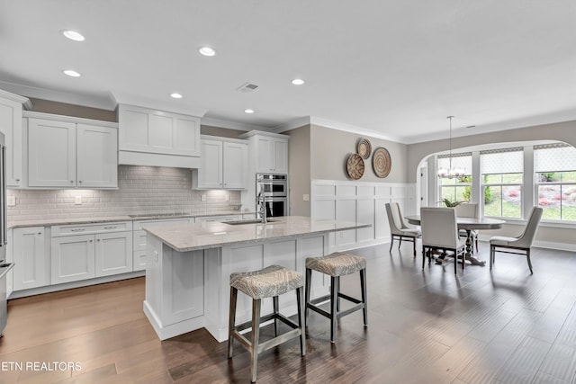 kitchen with white cabinets, wood finished floors, visible vents, and backsplash