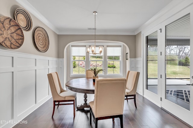 dining area featuring ornamental molding, arched walkways, an inviting chandelier, a decorative wall, and dark wood-style flooring