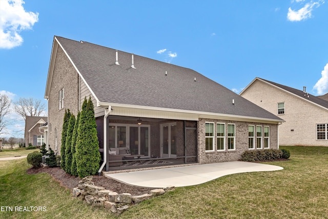 rear view of property with a yard, a sunroom, a shingled roof, a patio area, and brick siding