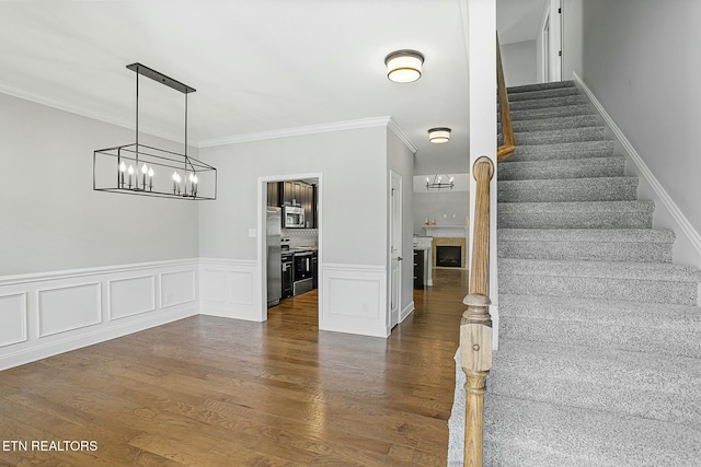 stairs with wainscoting, ornamental molding, an inviting chandelier, and wood finished floors