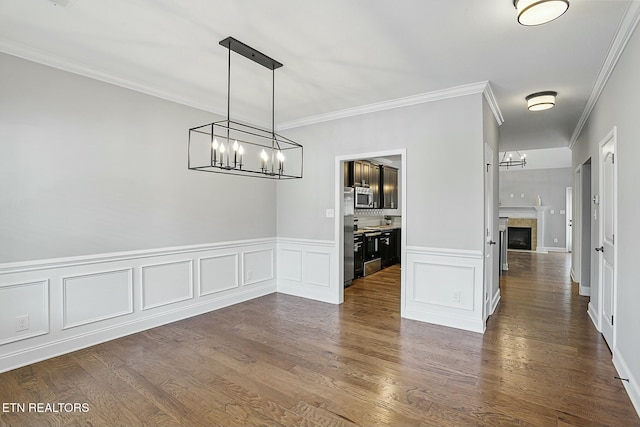 unfurnished dining area featuring crown molding, an inviting chandelier, dark wood-style flooring, and a tile fireplace