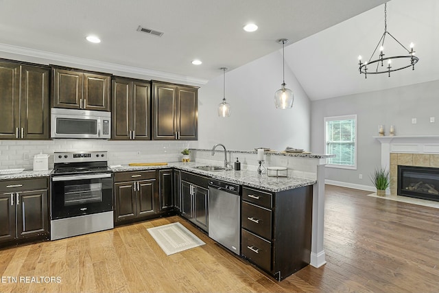 kitchen with a sink, light wood-style floors, appliances with stainless steel finishes, a peninsula, and light stone countertops