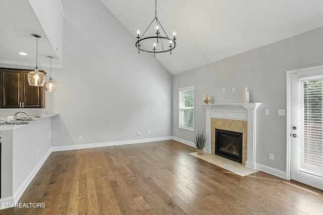 unfurnished living room with an inviting chandelier, wood finished floors, a healthy amount of sunlight, and baseboards