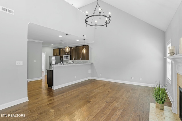 unfurnished living room with a tiled fireplace, visible vents, an inviting chandelier, and wood finished floors