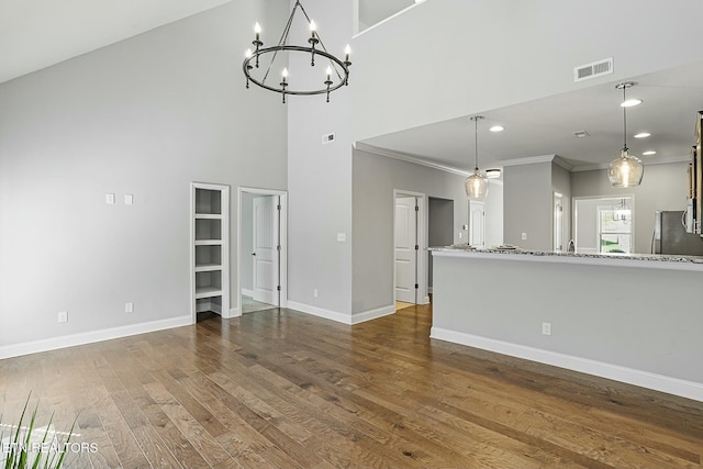 unfurnished living room featuring visible vents, a notable chandelier, ornamental molding, dark wood finished floors, and baseboards