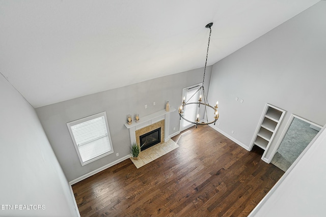 unfurnished living room with wood finished floors, baseboards, lofted ceiling, a tile fireplace, and a notable chandelier