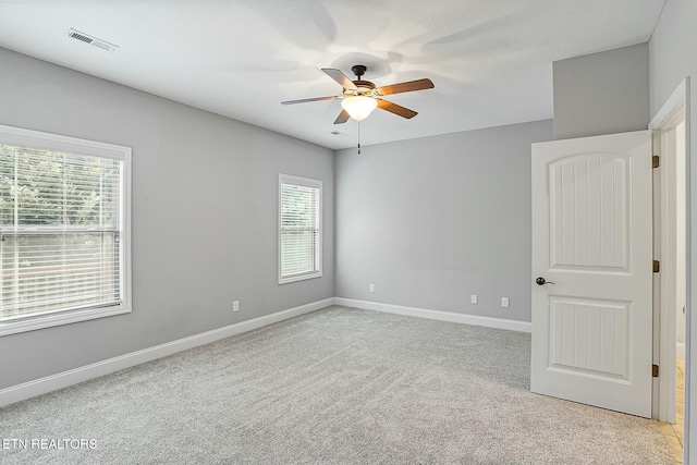 unfurnished room with light carpet, visible vents, baseboards, and ceiling fan