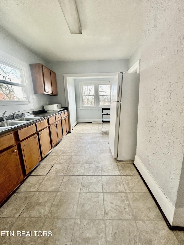 kitchen with brown cabinets, a sink, dark countertops, freestanding refrigerator, and a textured wall