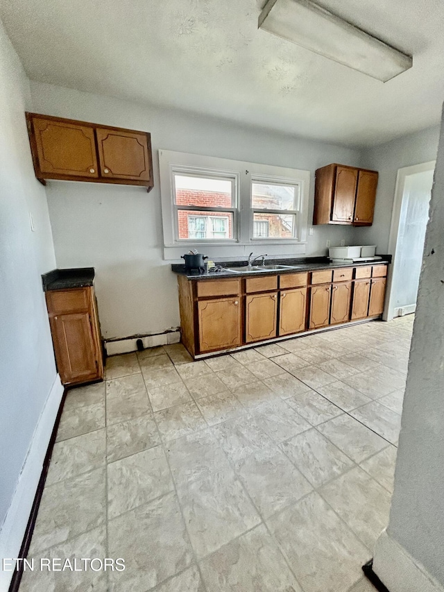 kitchen featuring dark countertops, baseboards, brown cabinets, and a sink