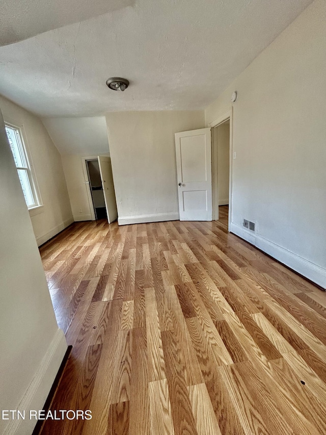 empty room with visible vents, lofted ceiling, a textured ceiling, wood finished floors, and baseboards