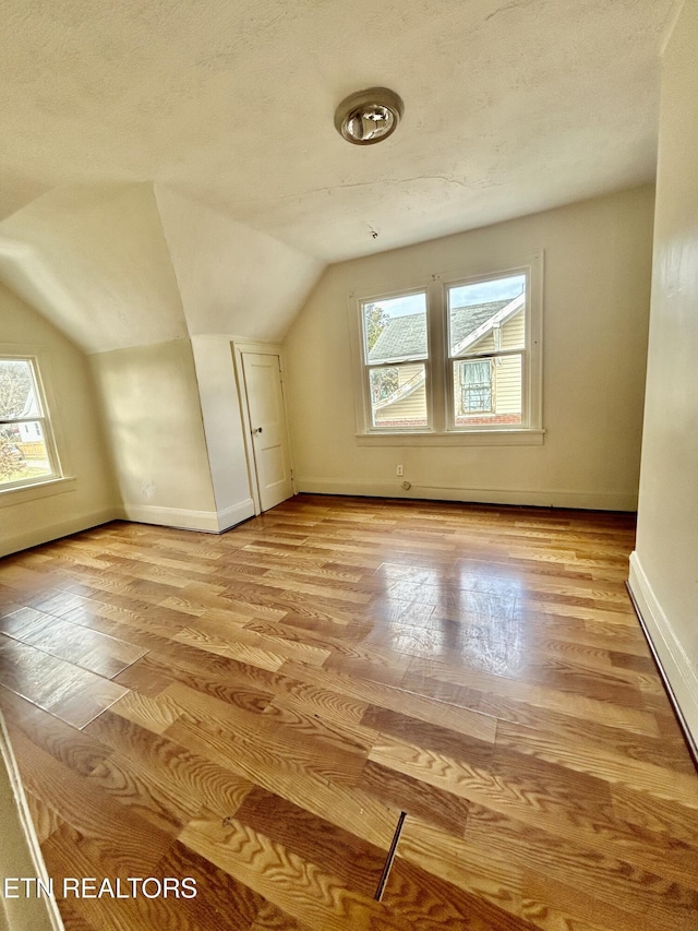 additional living space featuring light wood-style flooring, a textured ceiling, baseboards, and vaulted ceiling