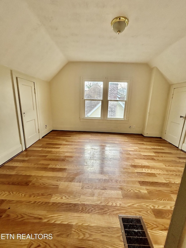 additional living space featuring visible vents, baseboards, lofted ceiling, and light wood-style floors