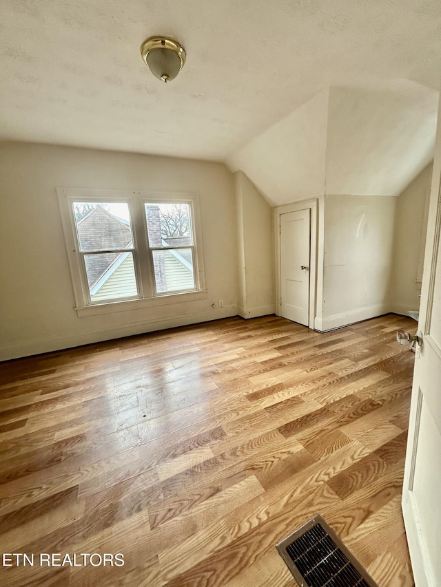 additional living space featuring visible vents, baseboards, lofted ceiling, and light wood-style floors