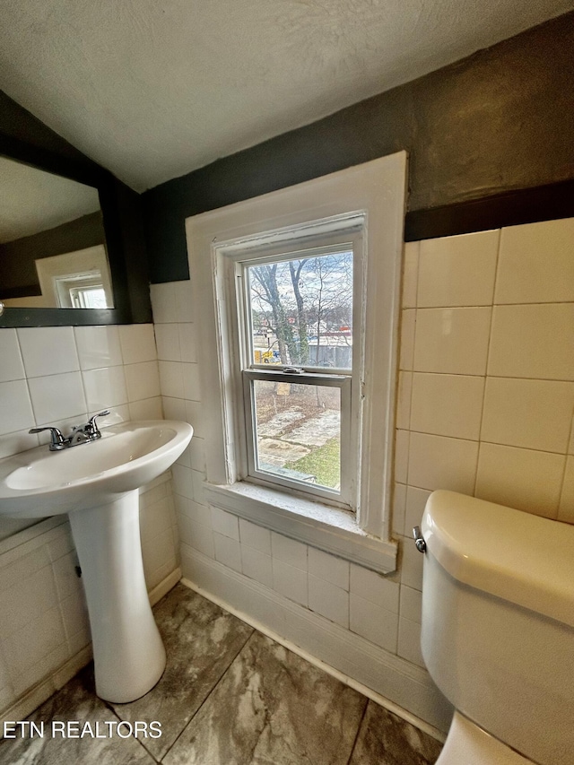 bathroom featuring toilet, a textured ceiling, and tile walls