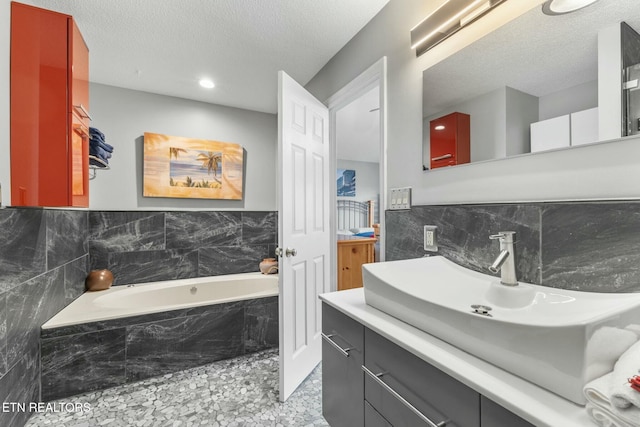 bathroom with a garden tub, a textured ceiling, tile walls, and vanity