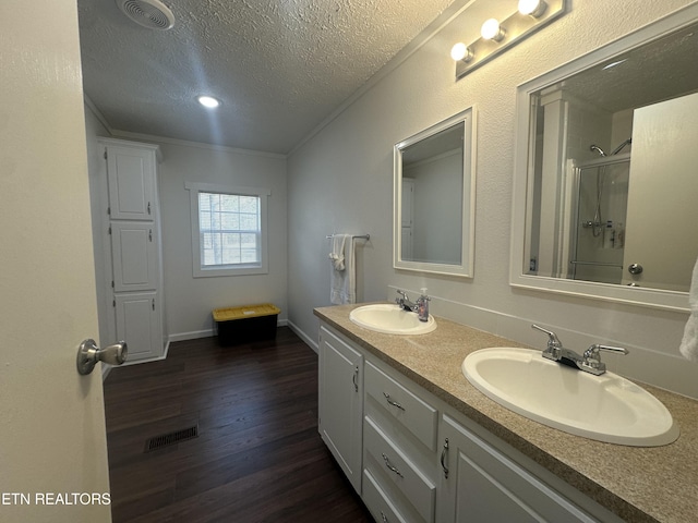 full bath featuring visible vents, a shower with shower door, wood finished floors, and a sink