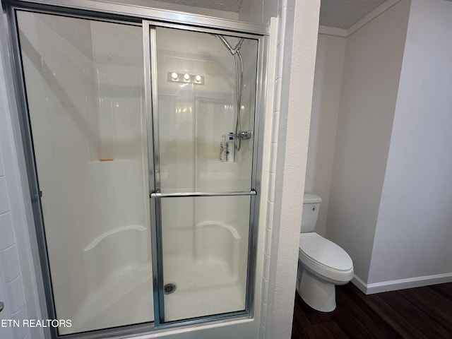 bathroom with toilet, wood finished floors, and a stall shower