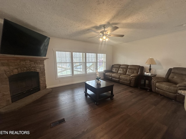 living room featuring a ceiling fan, dark wood-style floors, visible vents, baseboards, and a stone fireplace