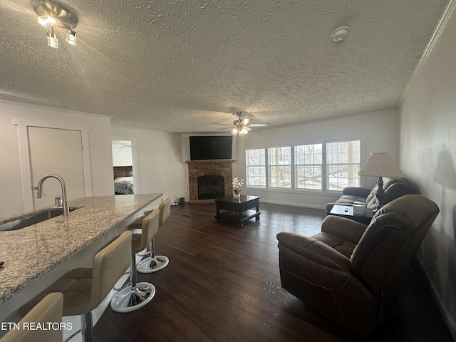 living area with dark wood-style floors, baseboards, a fireplace with raised hearth, ceiling fan, and a textured ceiling