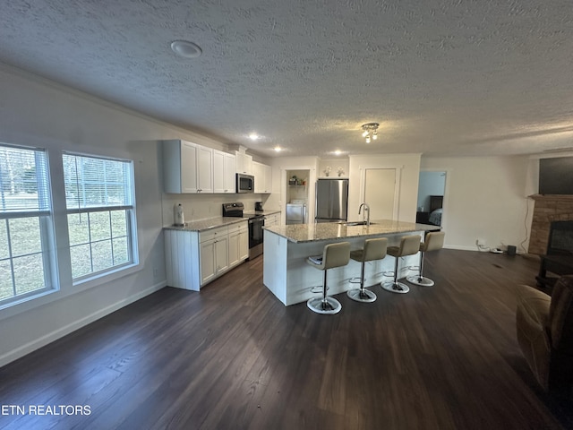 kitchen with a breakfast bar, light stone counters, appliances with stainless steel finishes, white cabinets, and dark wood-style flooring