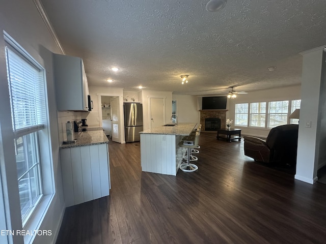 kitchen featuring a glass covered fireplace, dark wood-type flooring, a breakfast bar area, and freestanding refrigerator