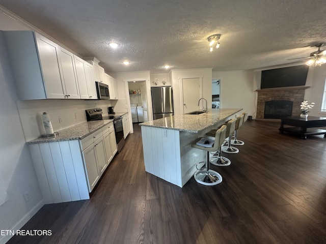 kitchen featuring a breakfast bar area, light stone countertops, a sink, dark wood-type flooring, and appliances with stainless steel finishes